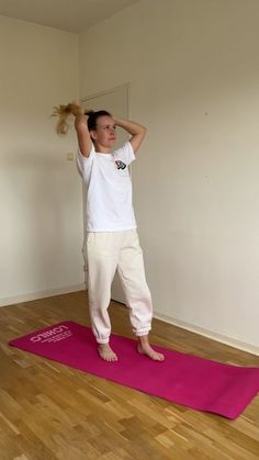 a woman standing on a pink yoga mat with her hands behind her head and arms in the air