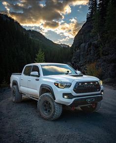 a white toyota pickup truck parked on the side of a mountain road at sunset with clouds in the sky