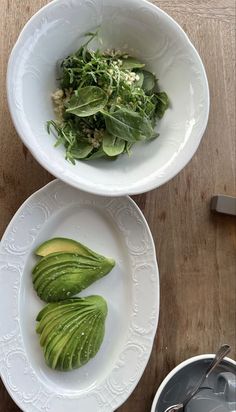 two white bowls filled with green vegetables on top of a wooden table next to utensils