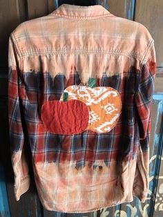 an orange and black plaid shirt with a patch on the chest, sitting against a wooden door