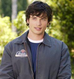 a young man standing in front of some trees and bushes with his hands on his hips