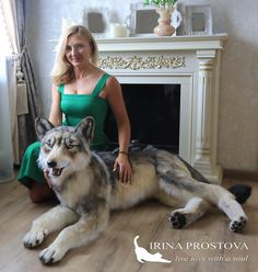 a woman in a green dress sitting on the floor next to a large wolf statue