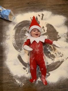 a baby wearing an elf costume laying on top of flour