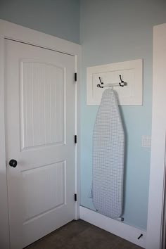 an ironing board is hanging on the wall in front of a door with hooks