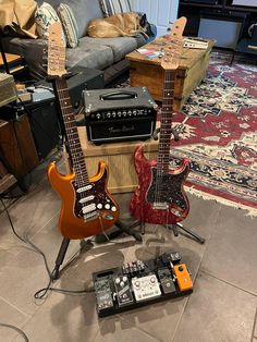 two electric guitars sitting on top of a floor next to a couch and guitar amp