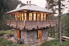 a small stone cabin in the woods with lights on and windows lit up at night