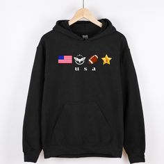 This USA Patriotic Hoodie is a perfect blend of American pride and love for sports. Featuring bold graphics of the American flag, a soaring eagle, a football, and a gold star, this hoodie symbolizes everything from national pride to the spirit of teamwork and athleticism. Whether you're cheering for your favorite team, celebrating the 4th of July, or simply showing off your love for the USA, this sweatshirt makes a bold statement. Made from high-quality, soft material, it offers warmth and comfort for everyday wear or during those chilly game nights. Ideal for sports fans, military supporters, and anyone who wants to proudly represent the red, white, and blue. A great addition to any patriotic wardrobe! This unisex heavy blend hooded sweatshirt is relaxation itself. Made with a thick blend Patriotic Crew Neck T-shirt For Fans, Patriotic Graphic Print Sweatshirt, American Style Crew Neck T-shirt With Flag Print, Eagle Football, American Flag Sweatshirt, Usa Hoodie, Soaring Eagle, American Flag Hoodie, Star Graphic