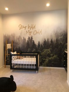 a baby's room with a crib and forest mural on the wall behind it