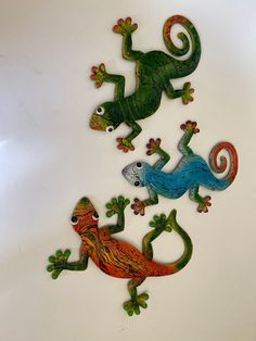 three metal geckos on a white surface with green and red ones in the middle