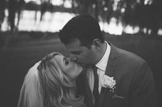 a bride and groom kissing in front of trees on their wedding day, black and white photo