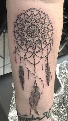 a woman's leg with a black and white dream catcher tattoo on the thigh