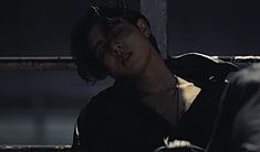 a young man with sunglasses resting on a bench in the dark, wearing a black shirt