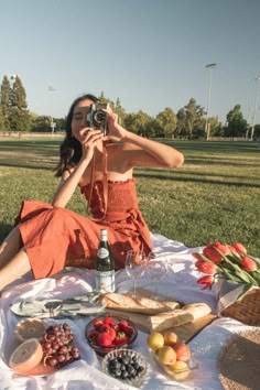 a woman sitting in the grass taking a photo with her camera and food spread out