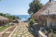 a stone path leads to thatched huts by the ocean