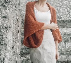 a woman standing in front of a stone wall with her arms crossed and looking at the camera