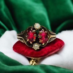 a red ring sitting on top of a green velvet covered cushion in front of a white blanket