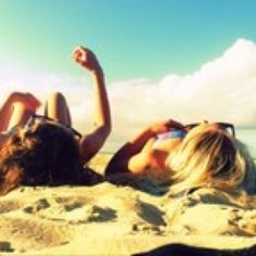 two women laying in the sand with their arms up and one holding a cell phone