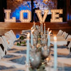 the table is set with white chairs and lit up love letters above it, along with candles