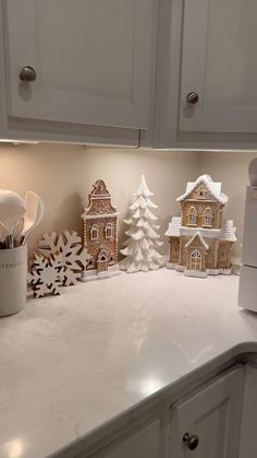 a white kitchen counter topped with lots of snow covered houses and small christmas trees on top of it