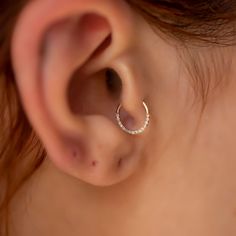 a woman's ear is shown with a small diamond hoop in the shape of a crescent