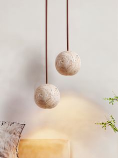 two white balls hanging from the ceiling next to a plant in a vase and chair