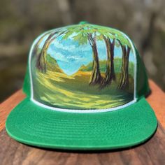 a green hat with trees painted on the front and sides, sitting on top of a wooden table