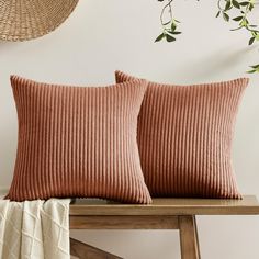 two pillows sitting on top of a wooden table next to a basket and potted plant