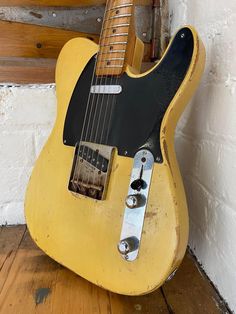 an old yellow guitar sitting on top of a wooden floor