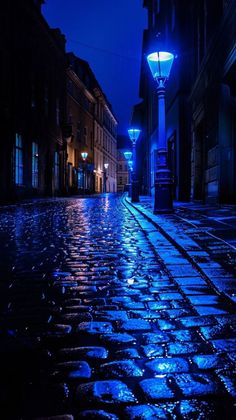 an empty cobblestone street at night with blue lights on the side and dark buildings in the background