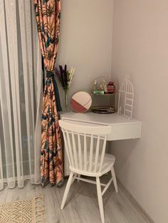 a white desk sitting next to a window in a room with sheer curtains on the windowsill