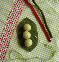 a green piece of fabric with two buttons on it and a red needle next to it