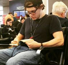 a man sitting in a chair with headphones on reading a book while others sit behind him