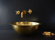 a gold sink with two faucets on the wall next to it and a black background