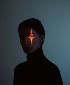 a woman with her face painted like a cross in the dark, looking at the camera