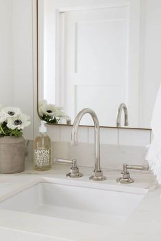 a white sink sitting under a bathroom mirror next to a vase with flowers on it