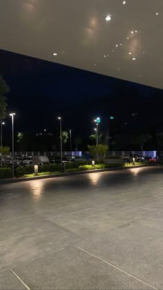 an empty parking lot at night with lights on the ceiling and street lamps in the background