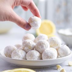 a person is picking up some food from a white plate with lemons on the side