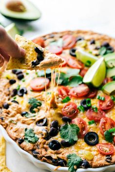 someone dipping tortilla into a dish with black olives, avocado and tomatoes