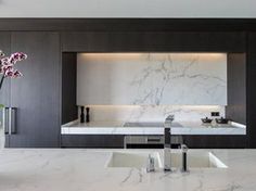 a modern kitchen with marble counter tops and black cabinets, along with a white vase filled with flowers