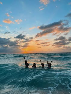 three people swimming in the ocean at sunset