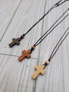 three wooden crosses hanging from a string on a white wood floor with bead necklaces