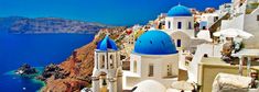 the blue domed buildings are on top of the hill by the water and cliffs in the background