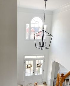 a chandelier hanging from the ceiling in a room with white walls and wooden stairs