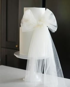 a white wedding cake with a sheer bow on the top is sitting on a table