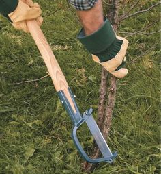 a man is holding a garden tool in his hand while standing next to a tree