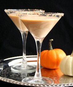 two glasses filled with liquid sitting on top of a silver tray next to small pumpkins