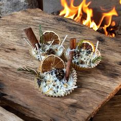 two cupcakes with orange slices and cinnamon sticks on a wooden table in front of a fire