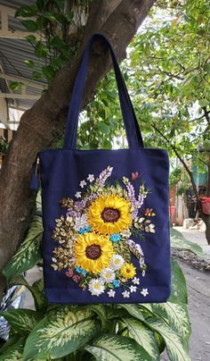 a blue bag with sunflowers and daisies on it hanging from a tree