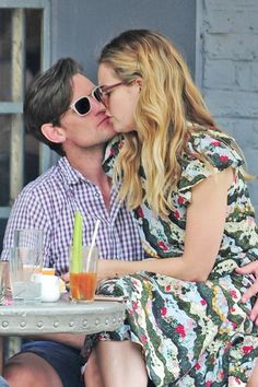 a man and woman kissing each other while sitting at a table with drinks in front of them