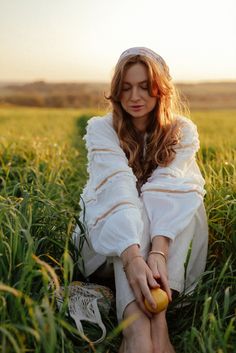 a woman sitting in the grass holding an apple